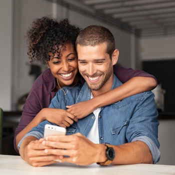 young couple embracing while looking at smartphone