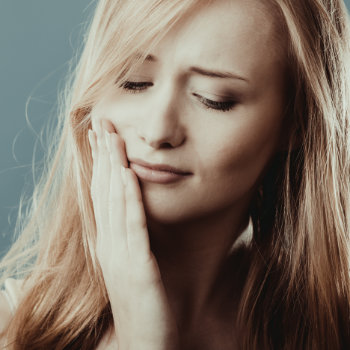 sad blond haired woman holding her cheek in pain