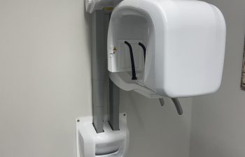 A dental panoramic X-ray machine is mounted on a gray wall in a clinical setting.