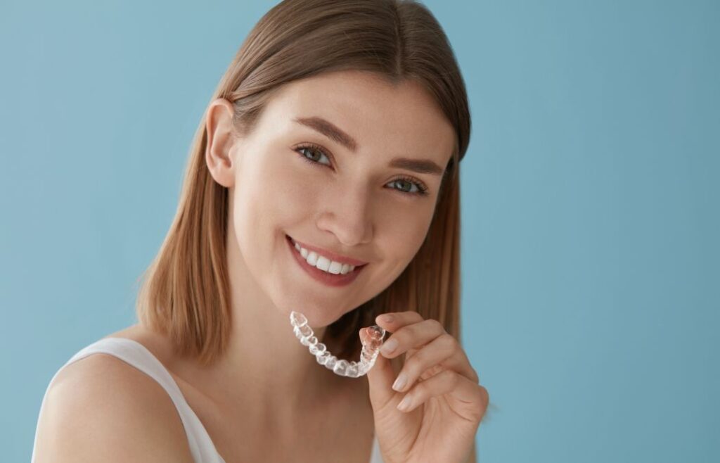 Smiling young woman with perfect teeth holding a clear orthodontic aligner
