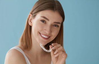 Smiling young woman with perfect teeth holding a clear orthodontic aligner