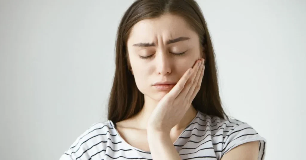 Woman holding cheek in pain from broken tooth seeking dental relief